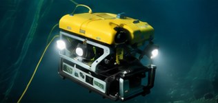 A yellow ROV with its lights on, filming a pipeline.